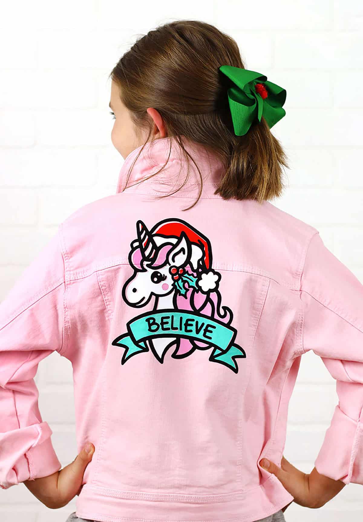 pink denim jacket with christmas unicorn design on back that reads believe