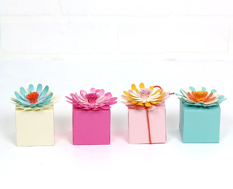 a line of four paper flower treat boxes in different colors in front of a white background