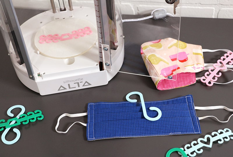 finished 3d printed ear savers pictured with cloth face masks and silhouette alta 3d printer
