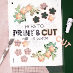 white cardstock on silhouette cutting mat with words printed and cut out of the cardstock reading how to print & cut with silhouette paper flowers and other craft supplies surround the cutting mat
