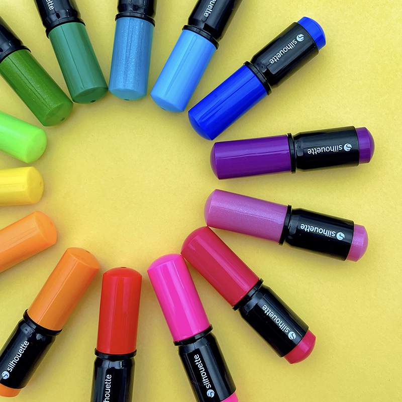 Silhouette sketch pens positioned in a rainbow circle formation on a pale yellow background.