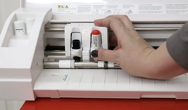 Hand putting a red Silhouette sketch pen into the second tool holder of a Silhouette Cameo 3.