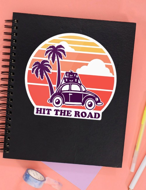Black notebook with road trip SVG design on the front picturing a car with suitcases on top and palm trees in front of a retro style sunset