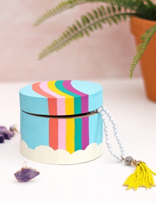Painting rainbow trinket box sitting on a white surface surrounded by colorful jewelry.