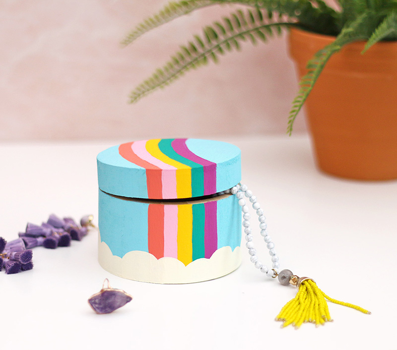 Painting rainbow trinket box sitting on a white surface surrounded by colorful jewelry.