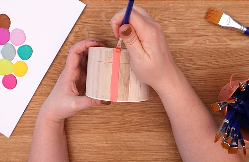 Painting a coral pink stripe on the side of a small wooden box.