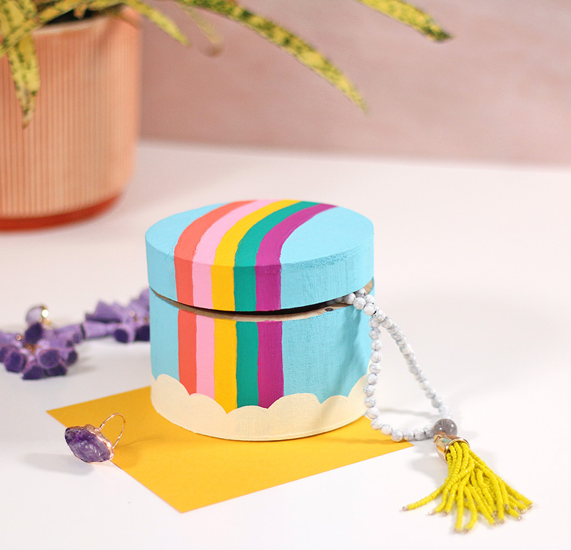 Painting rainbow trinket box sitting on a white surface surrounded by colorful jewelry.