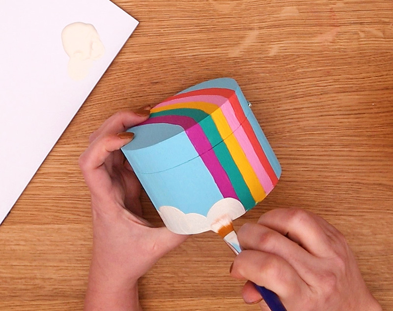 Painting a cloud border over the rainbow striped design on a wooden box.