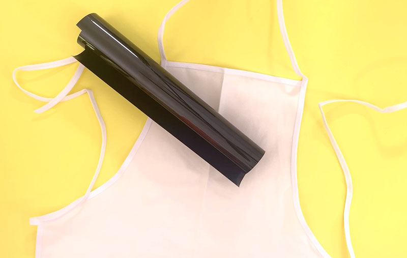 Blank white apron on yellow background with roll of black heat transfer vinyl.