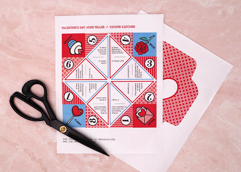Valentine Cootie Catcher printables printed out on white copy paper and sitting on light pink background with a pair of black scissors.