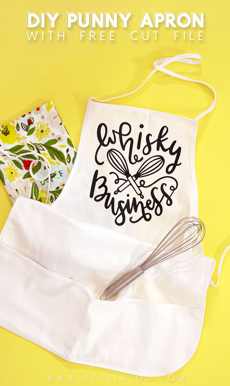 White apron on yellow background with black vinyl design that reads "Whisky Business" and includes a drawing of two whisks crossed. There is a floral fabric napkin below the apron and a metal whisk in the apron's pocket.
