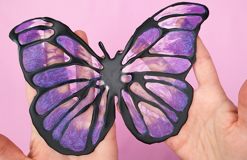 Hands holding butterfly window cling over pink background.