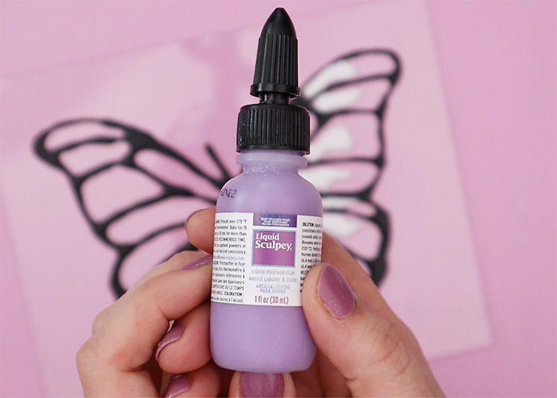 Hands holding bottle of multi-chromatic purple Liquid Sculpey.
